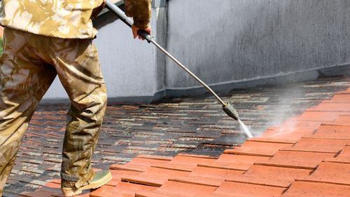 A man is cleaning a brick walkway with a high pressure washer.