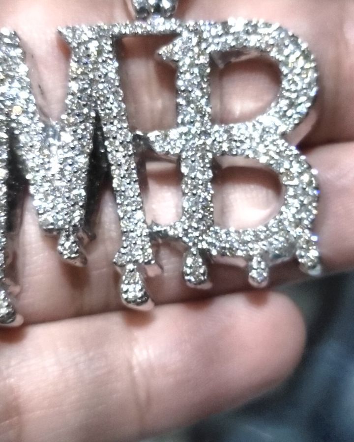 A person is holding a necklace with the letter mb on it