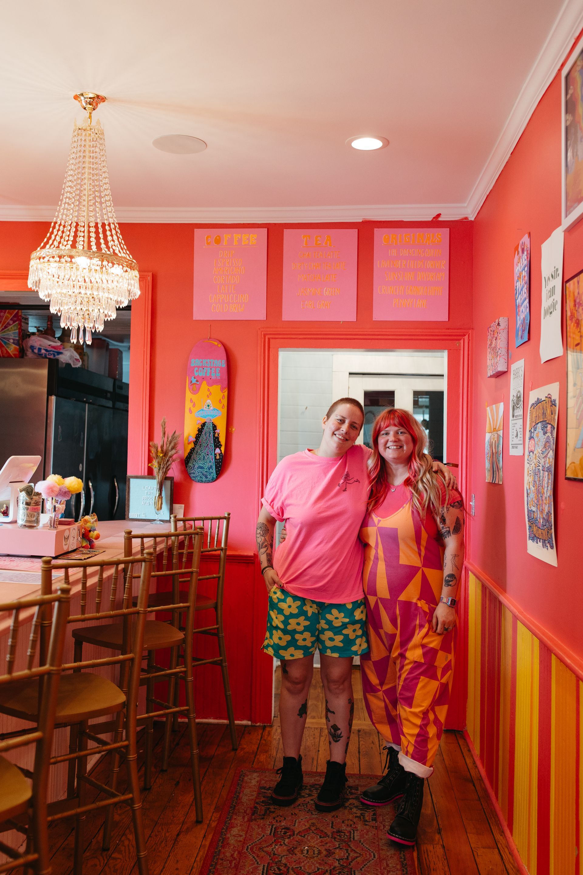 Two women are hugging in front of a fireplace with a sun on the wall behind them.