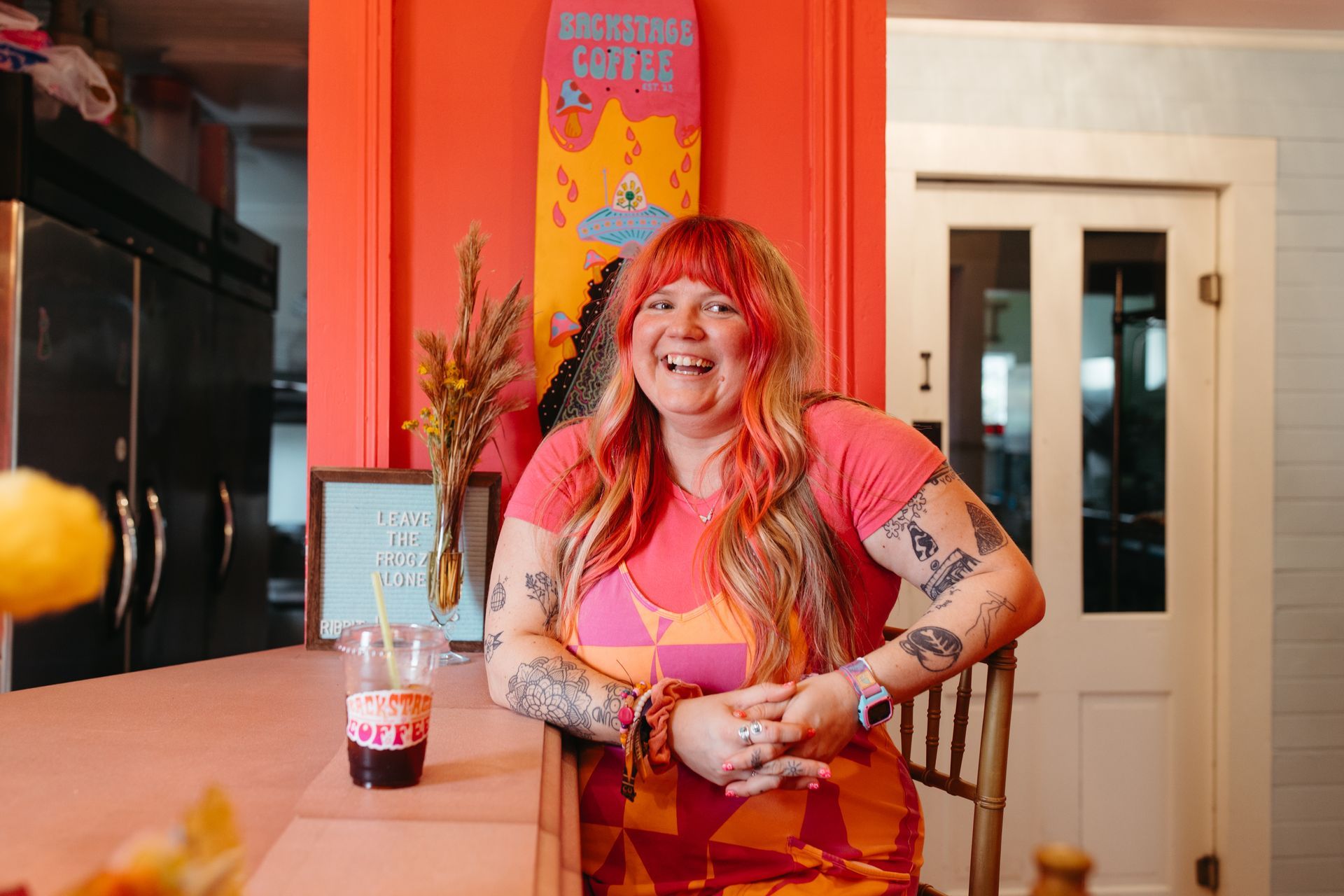 A woman in a pink shirt is sitting at a counter with a glass of liquid on it.