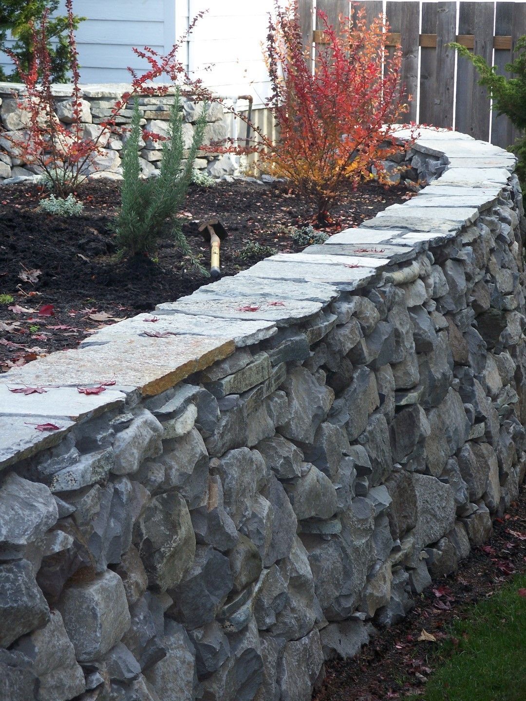 A stone wall in a garden with a fence in the background