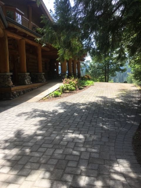 A brick driveway leading to a large log cabin surrounded by trees.