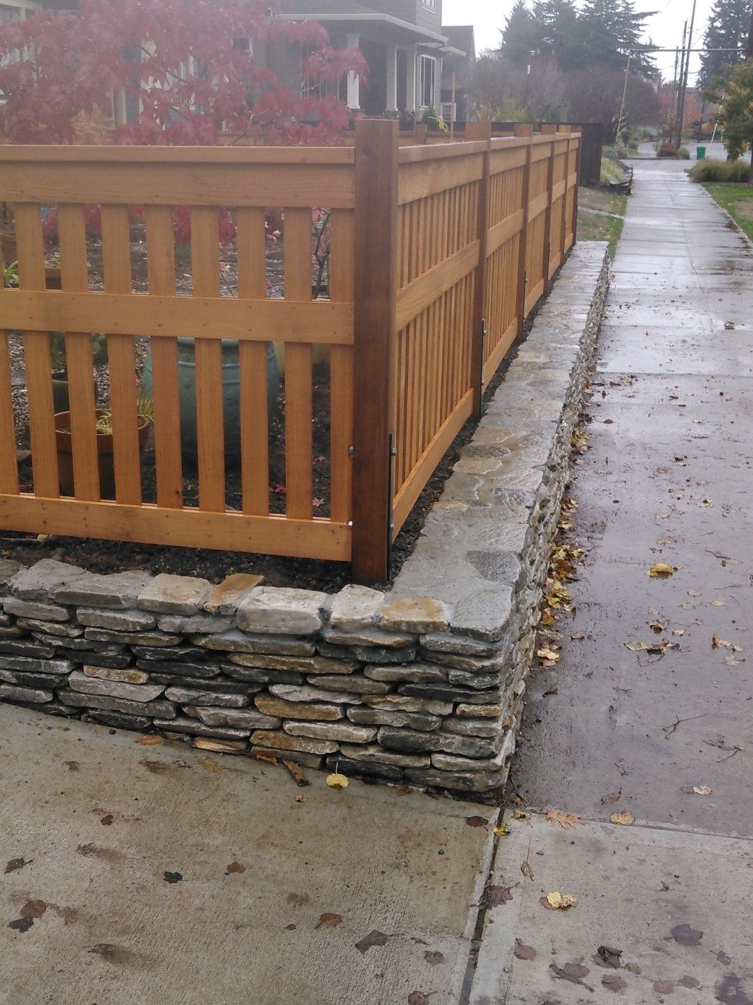 A wooden fence along a sidewalk next to a stone wall