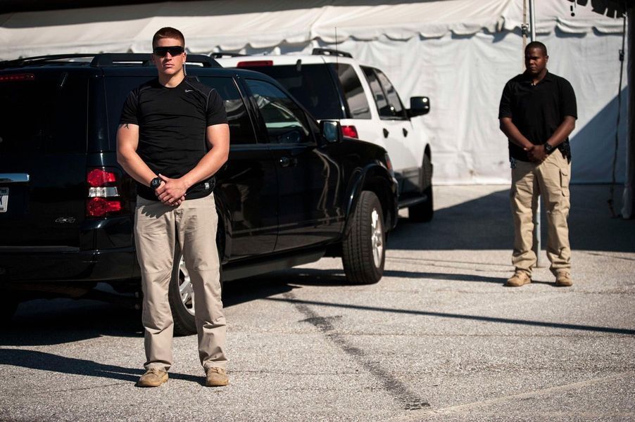 Two men are standing in front of a car in a parking lot.