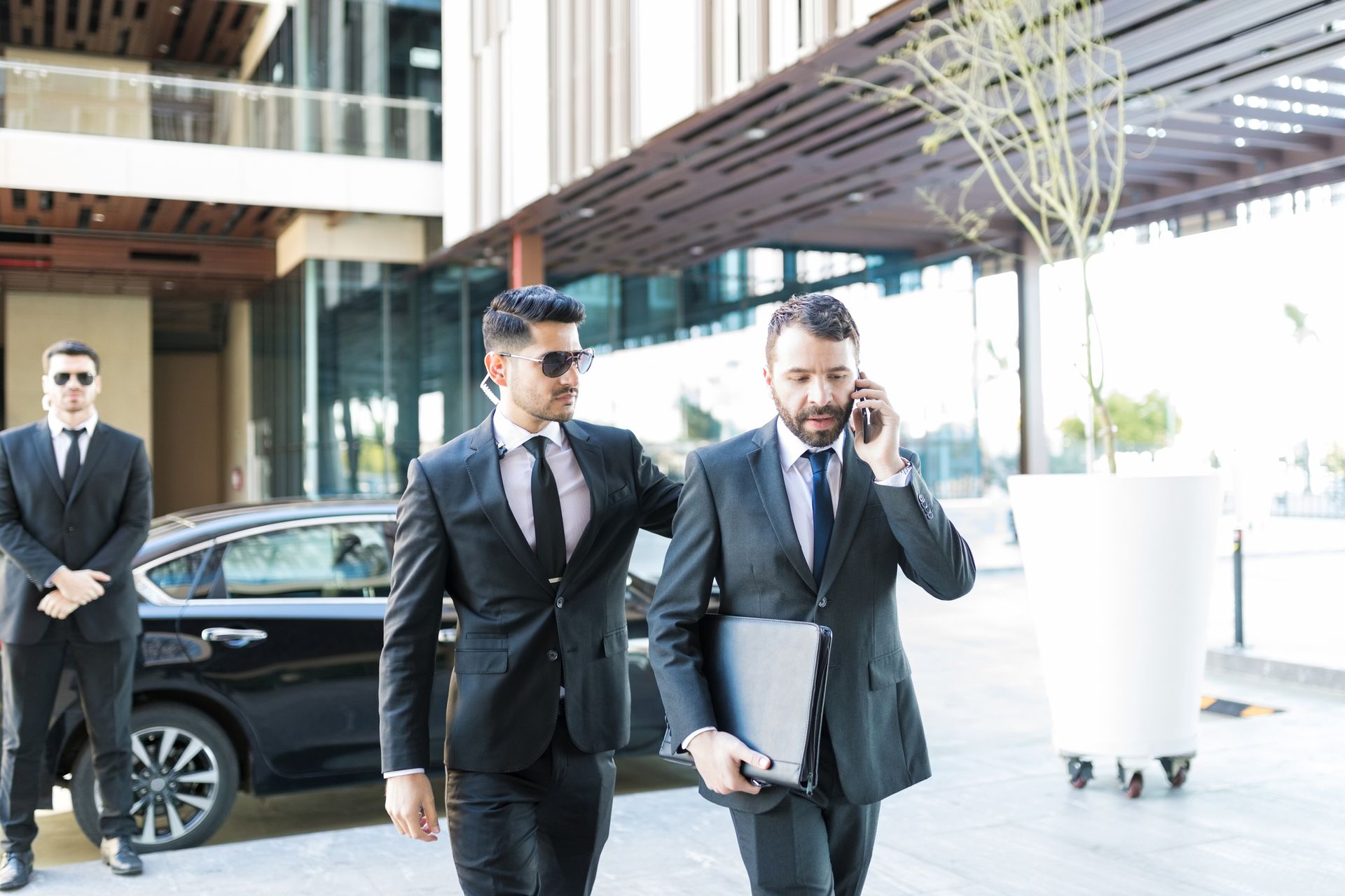 A man in a suit is talking on a cell phone while walking with two bodyguards.