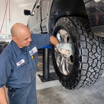 Mechanic in a Blue Uniform and Clear Gloves Cleans the Rim of a Large, Raised Truck Tire with a Cloth | Crown City Tire Auto Care