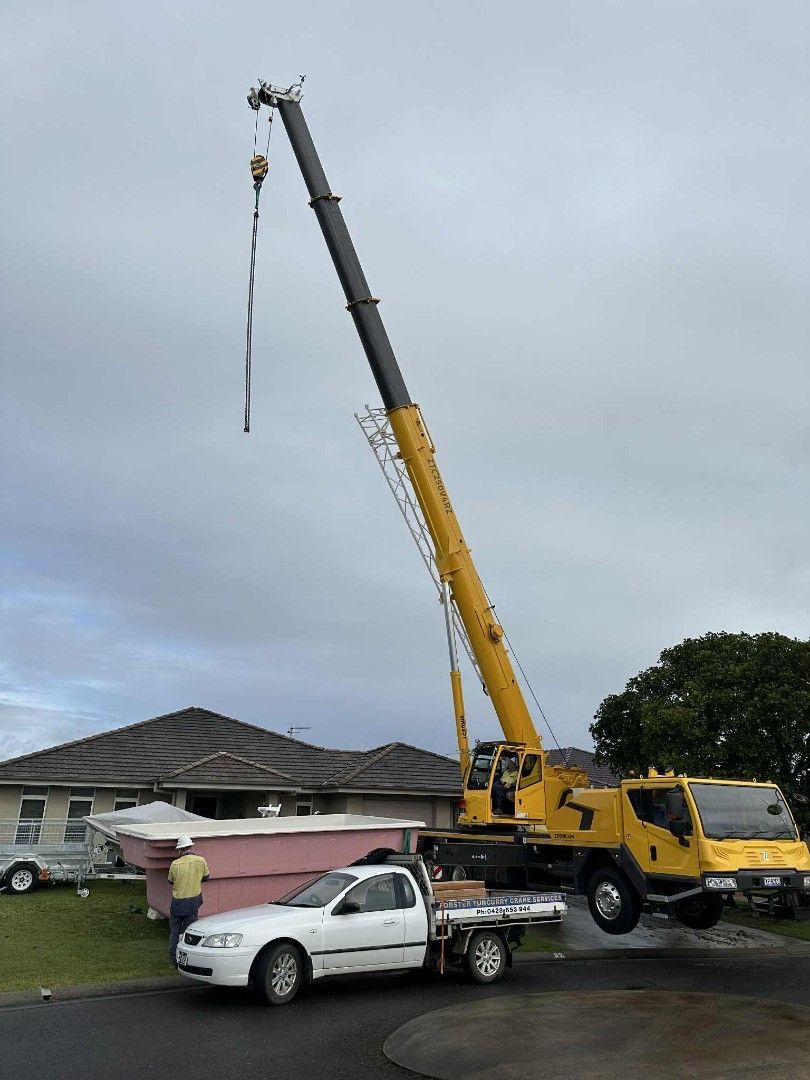 Yellow crane lifting a boat with a white pickup truck parked nearby under an overcast sky — Crane Rentals in Taree, NSW