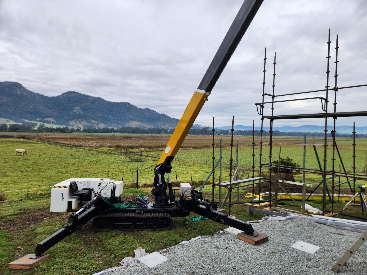 Yellow and black crawler crane on a worksite with scaffolding and a field in the background — Crane Rentals in Taree, NSW