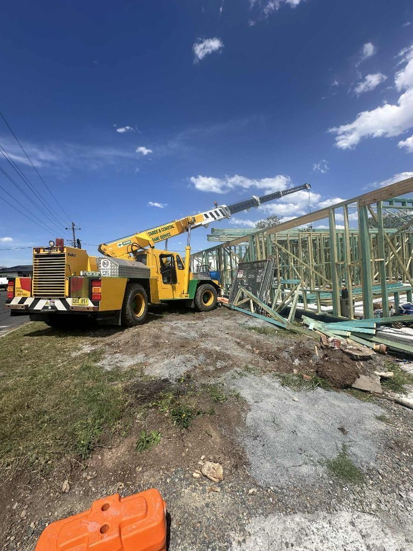 Yellow crane lifting wooden beams at a construction site on a sunny day — Crane Rentals in Taree, NSW