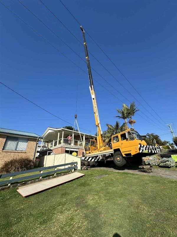 Yellow crane lifting object near a house with power lines overhead on a sunny day — Crane Rentals in Taree, NSW