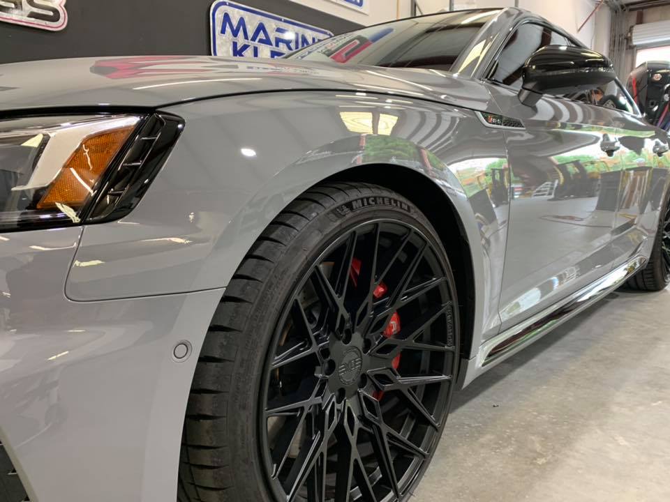 A close up of a gray car with black wheels in a garage.