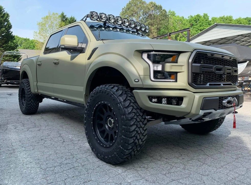 A green ford raptor is parked in a parking lot.