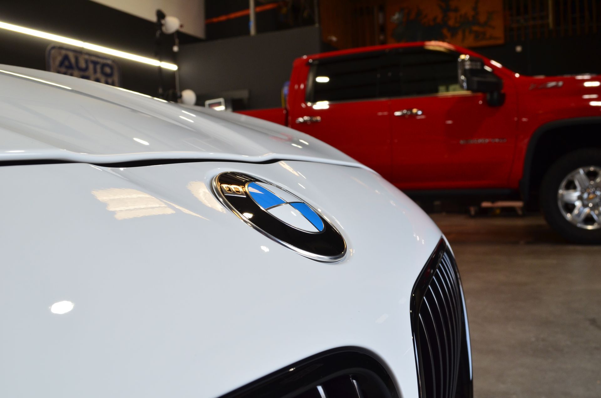 A white bmw is parked next to a red truck in a garage.