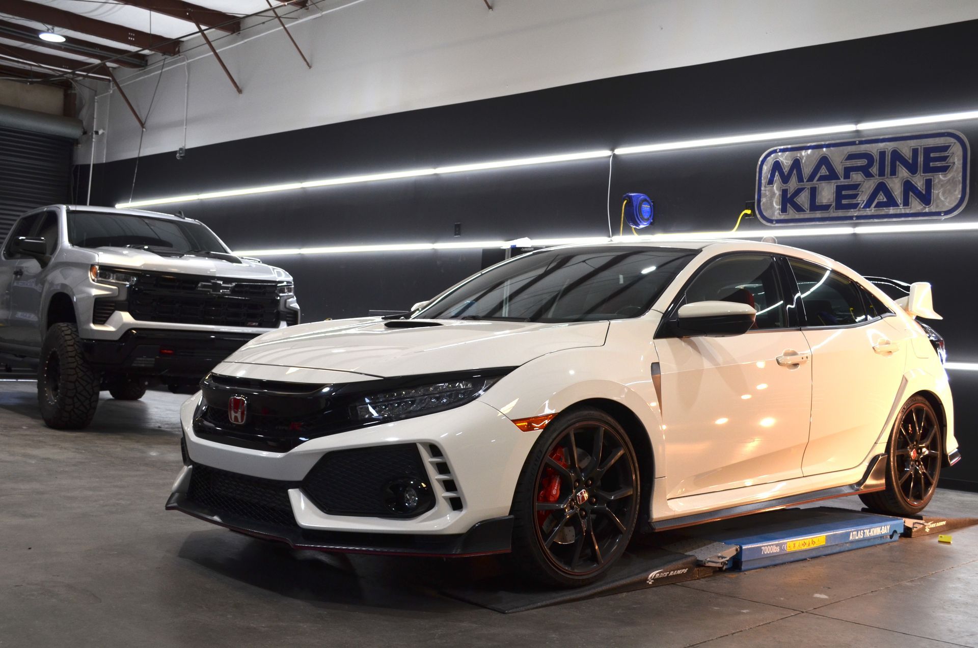 A white car is parked next to a white truck in a garage.