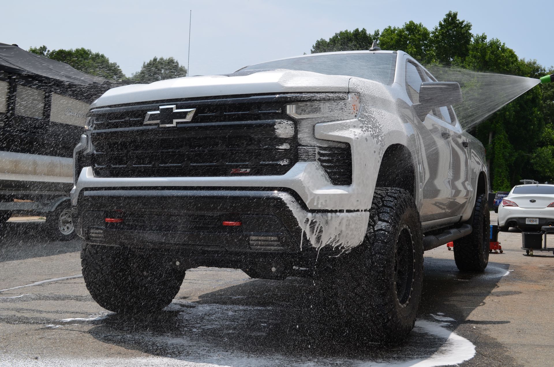 A white chevrolet truck is being washed in a parking lot.
