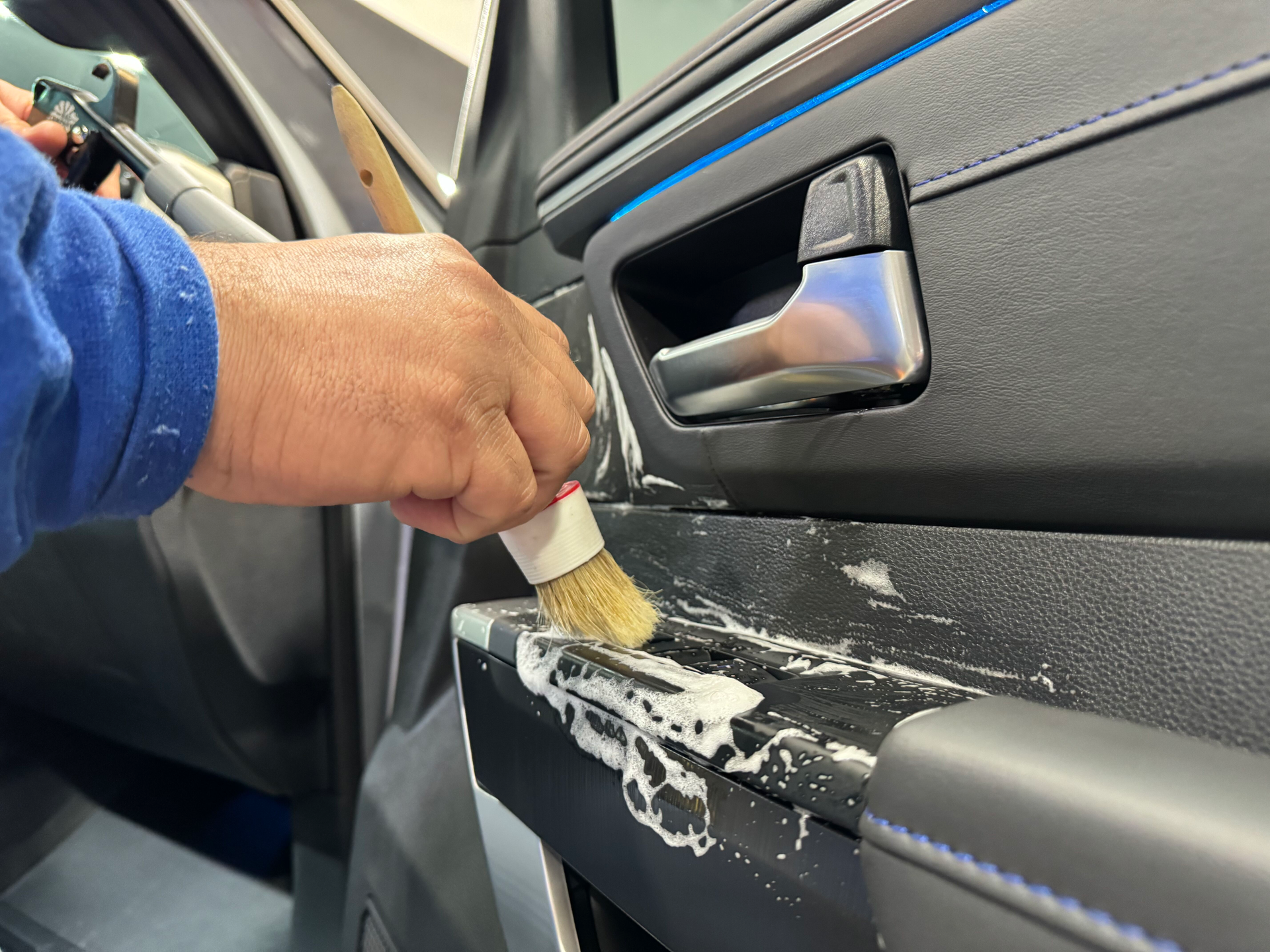 A person is cleaning a car door with a brush.