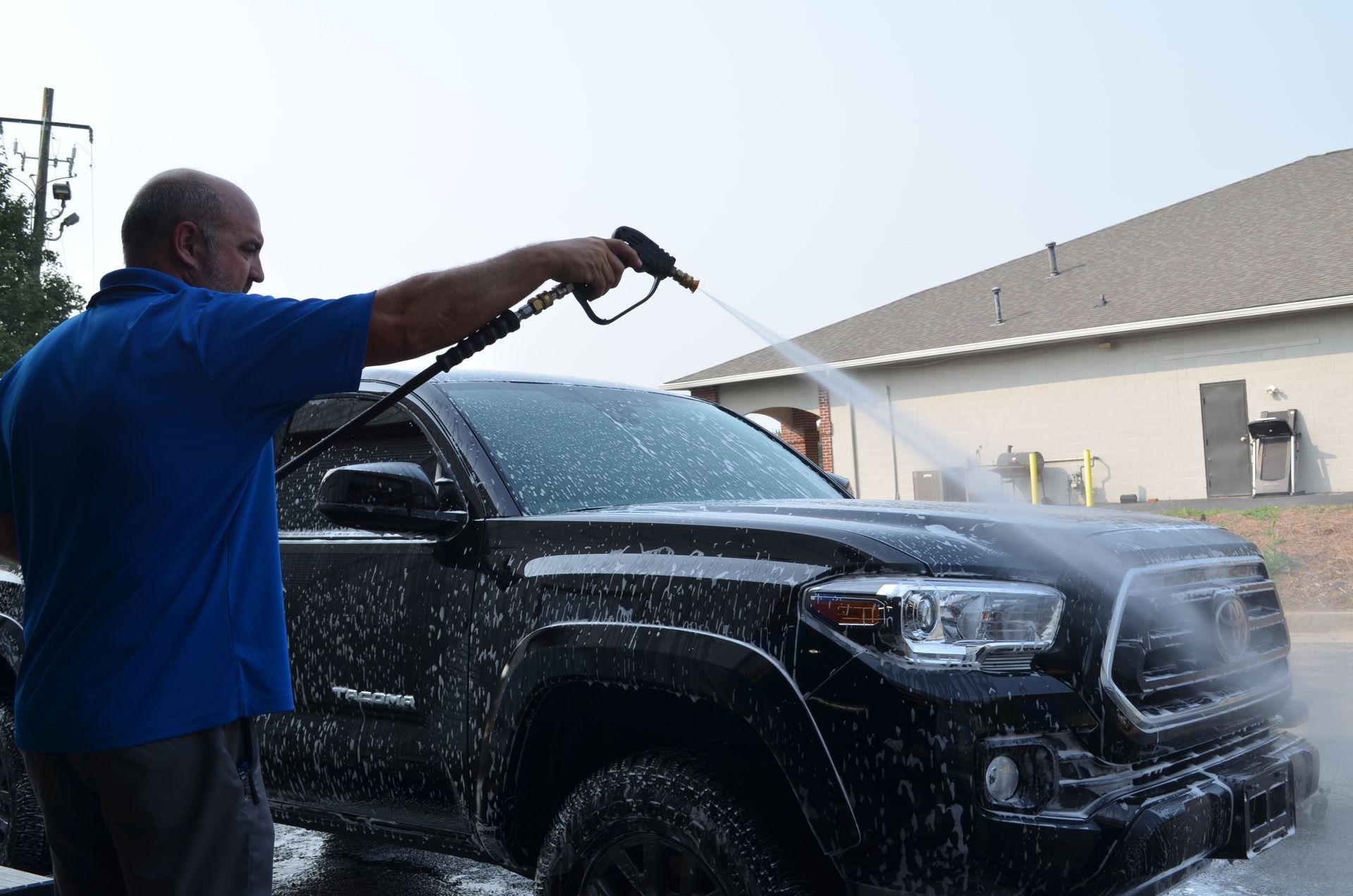 A man is washing a black truck with a high pressure washer.