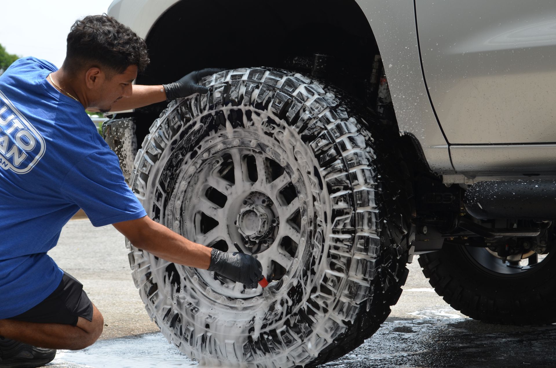 A man in a blue shirt is cleaning a tire with soap.