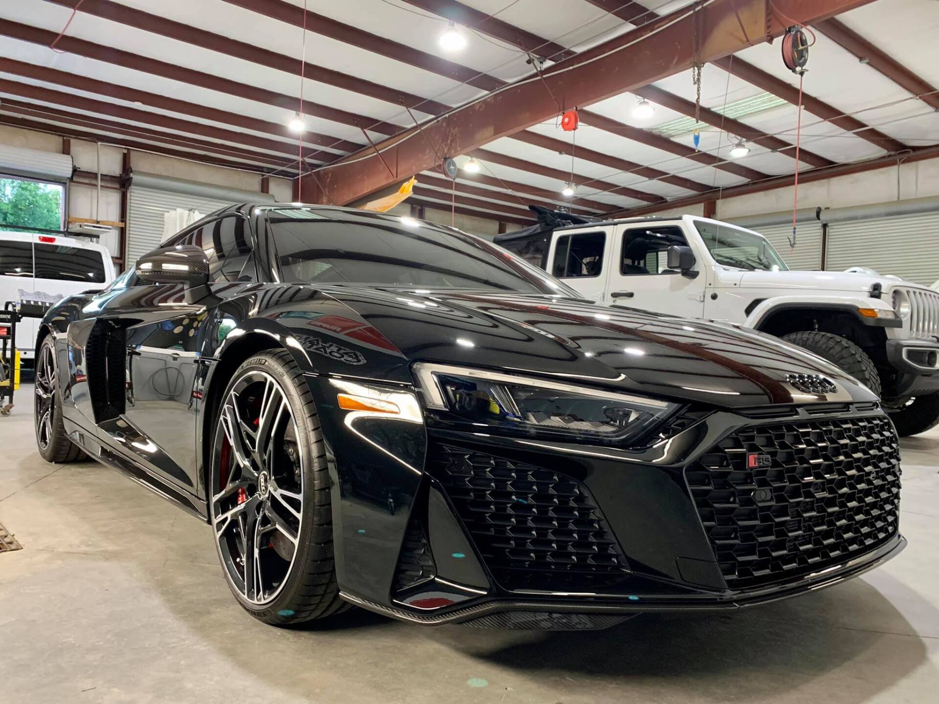 A black audi r8 is parked in a garage next to a white jeep.