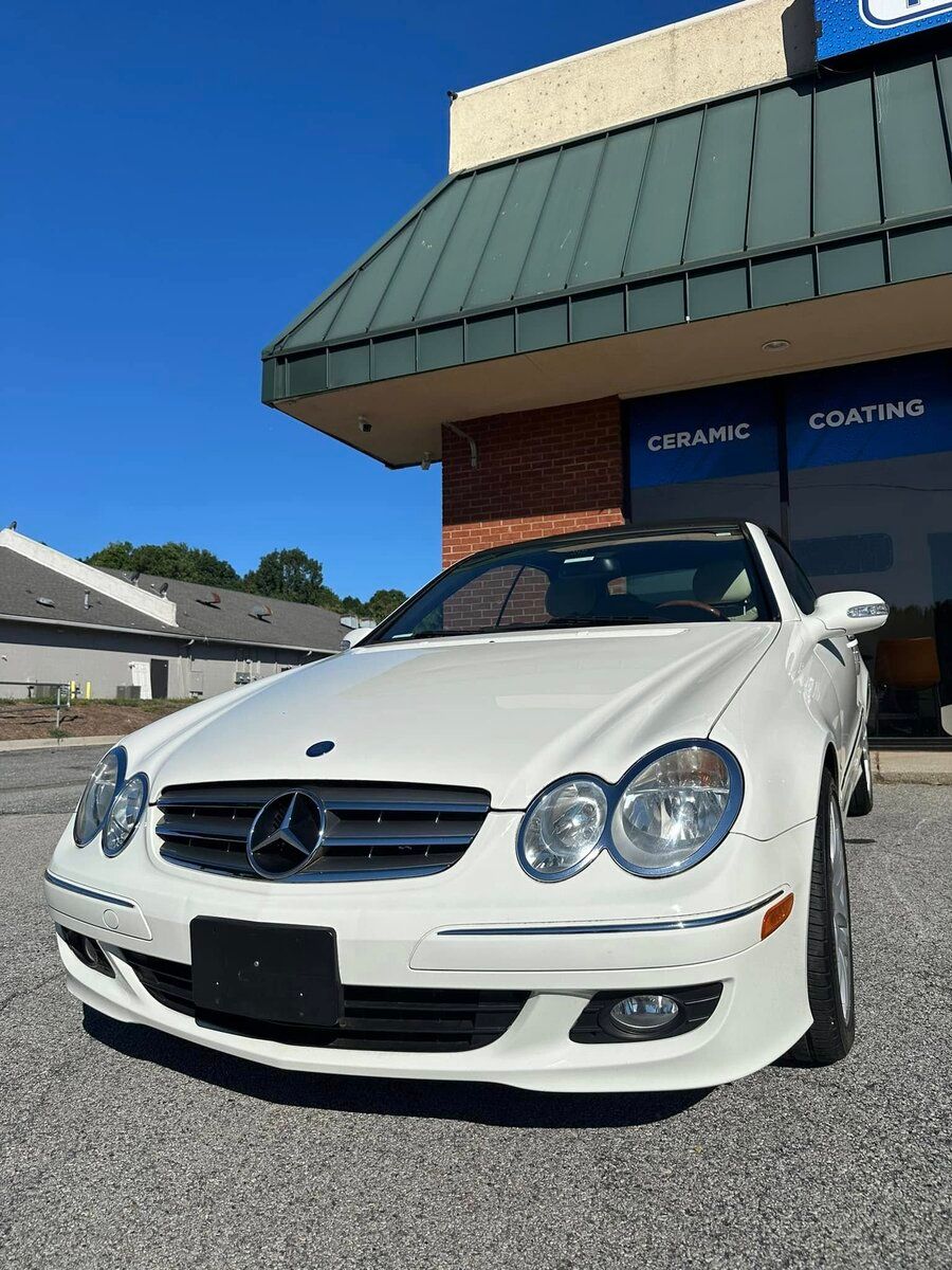 White Mercedes-Benz coupe parked in front of a building with a green awning. Blue sky.