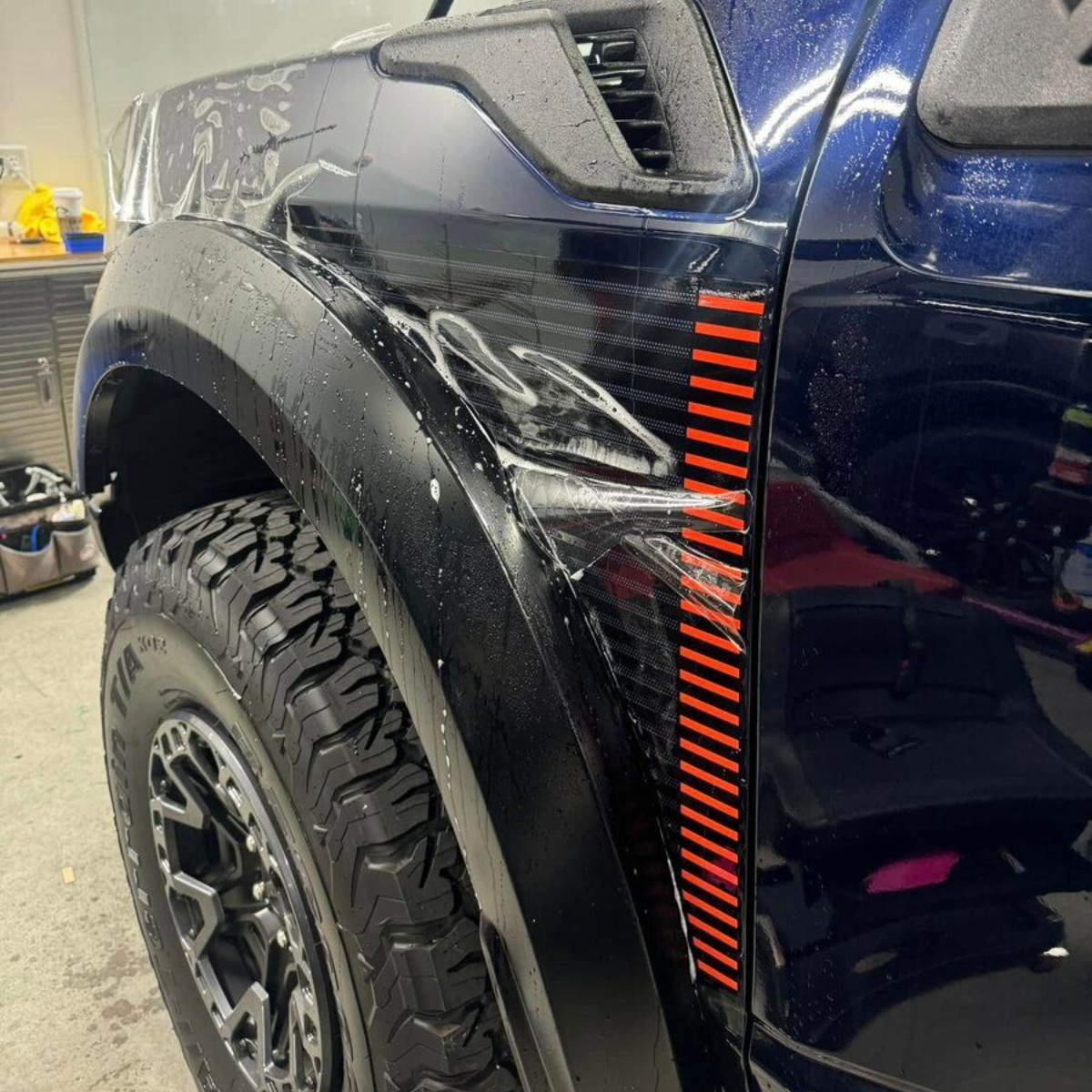 A white car is parked next to a white truck in a garage.