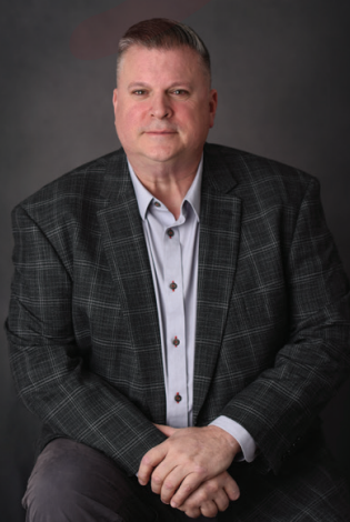 A man in a suit is sitting down with his hands folded.