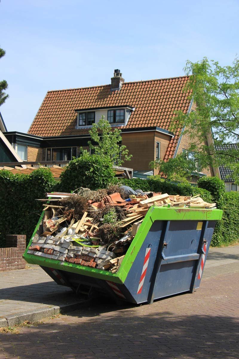 Blue and green dumpster overflowing with debris in front of a house.