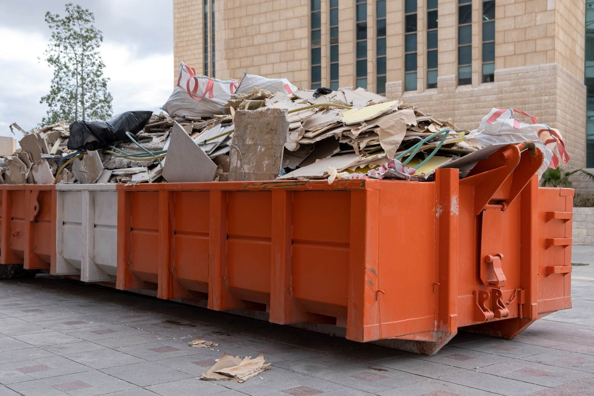 Orange and white dumpster overflowing with construction debris, parked outdoors.