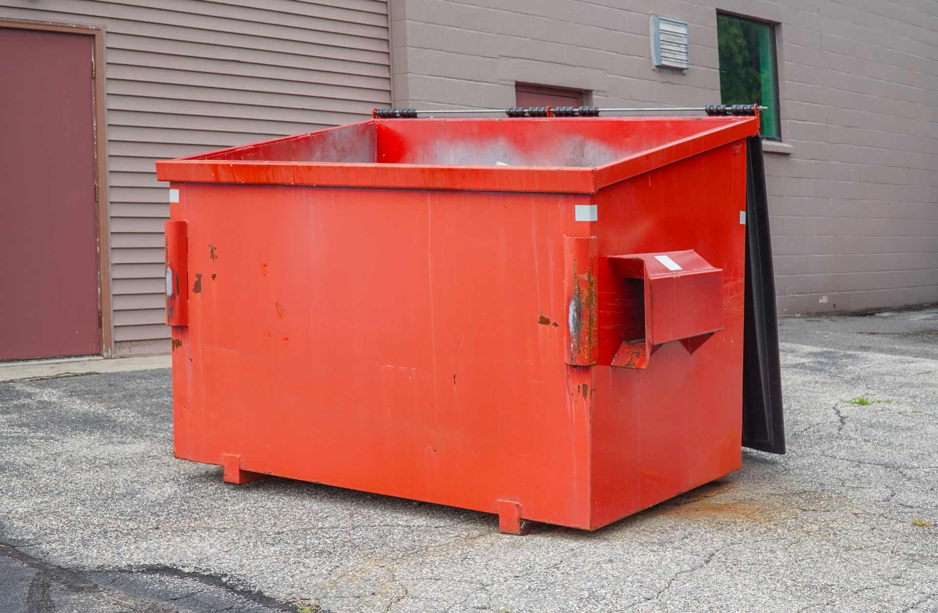 Red commercial dumpster outside a brick building.