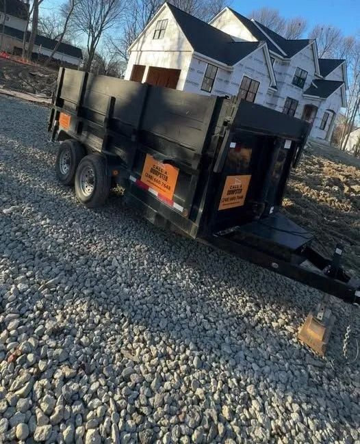 Black dump trailer on gravel in front of a house under construction.