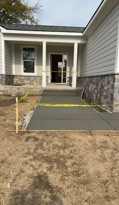 New concrete walkway leading to the front door of a light-colored house under construction. Yellow caution tape is present.