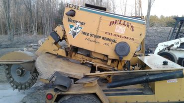 a yellow stump grinder that says ' della 's tree removal ' on it
