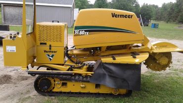 a yellow vermeer stump grinder is parked in the grass