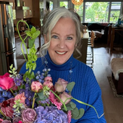 Smiling woman in a blue sweater holding a bouquet of pink and purple flowers indoors