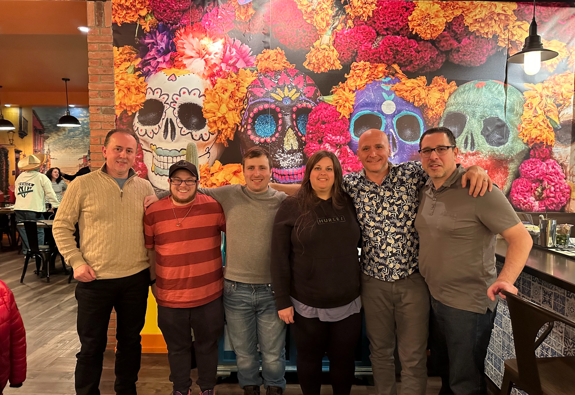 A group of people are posing for a picture in front of a wall with sugar skulls on it.