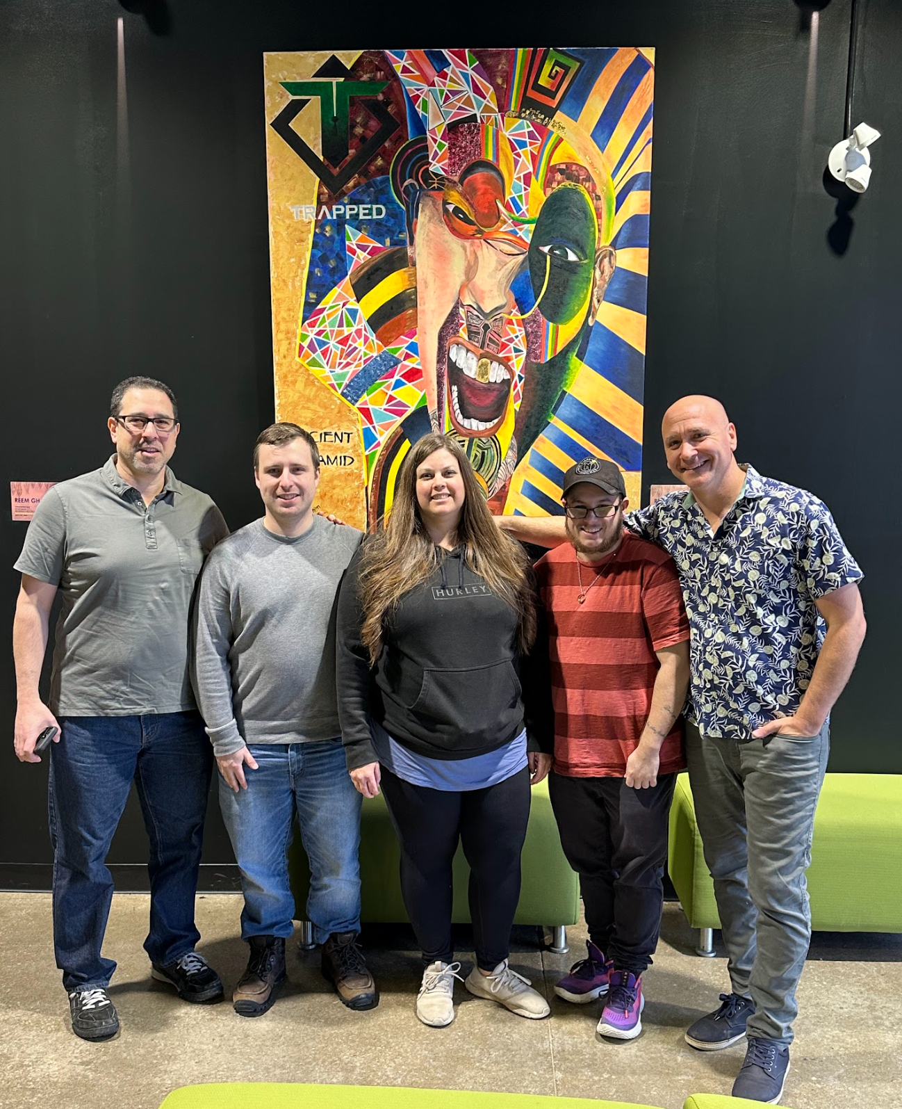 A group of people are posing for a picture in front of a painting.
