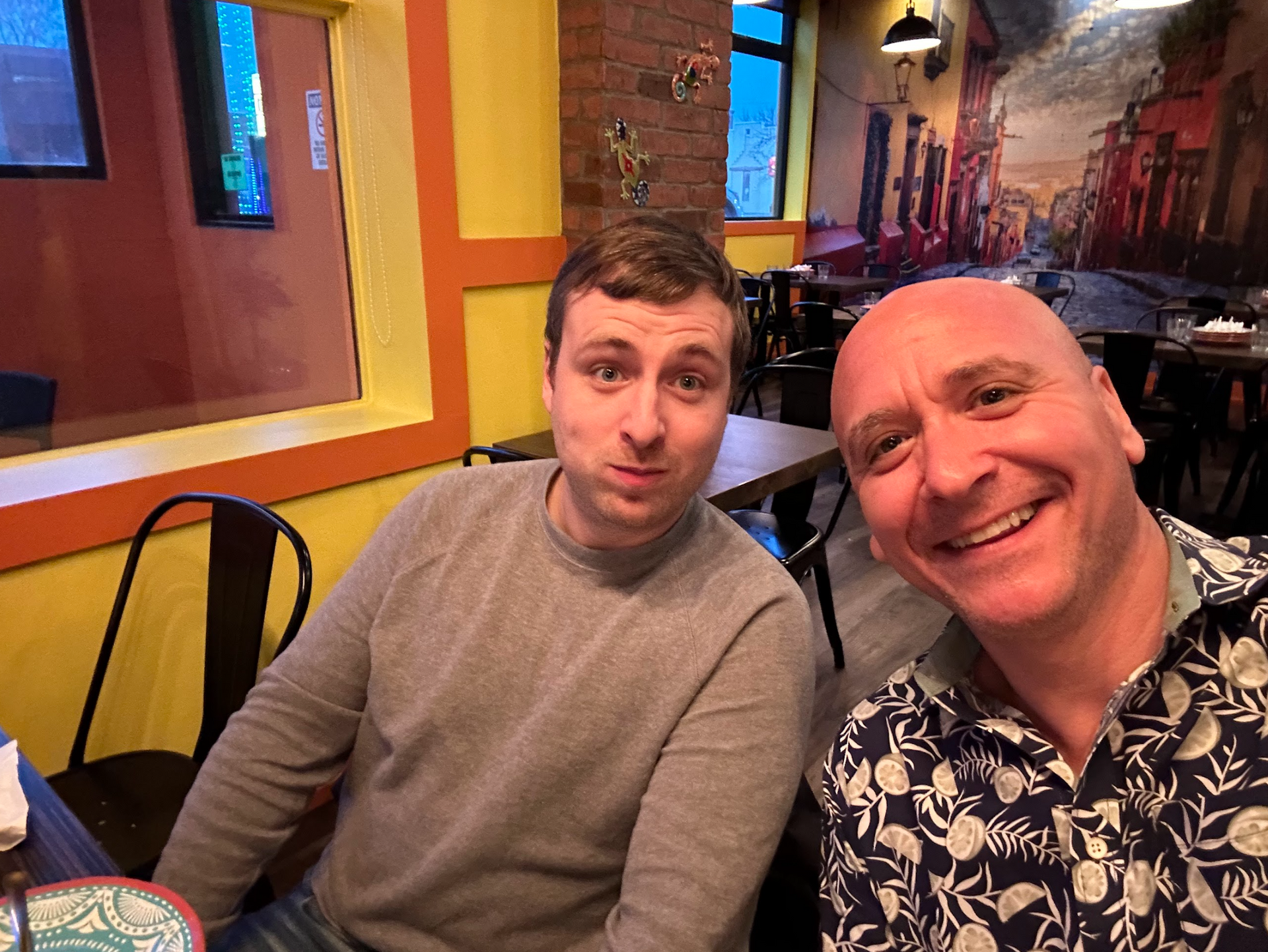 Two men are sitting at a table in a restaurant and smiling for a picture.