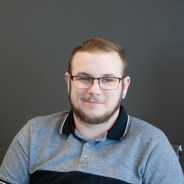 A man with glasses and a beard is wearing a gray and black polo shirt.