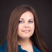 A woman with long brown hair and blue eyes is wearing a blue shirt.