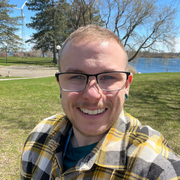 A man with glasses and a beard is wearing a gray and black polo shirt.