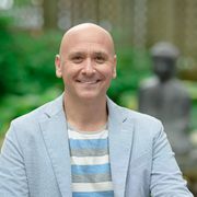 A bald man in a suit and striped shirt smiles for the camera