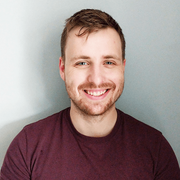 A man with a beard wearing a maroon shirt is smiling for the camera.