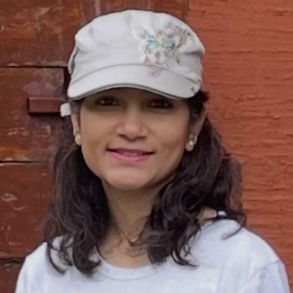 Smiling person in a white cap and shirt standing against a red brick wall
