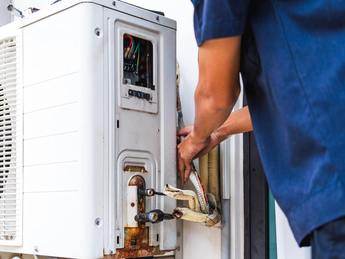 Person in blue shirt repairing an outdoor air conditioning unit.