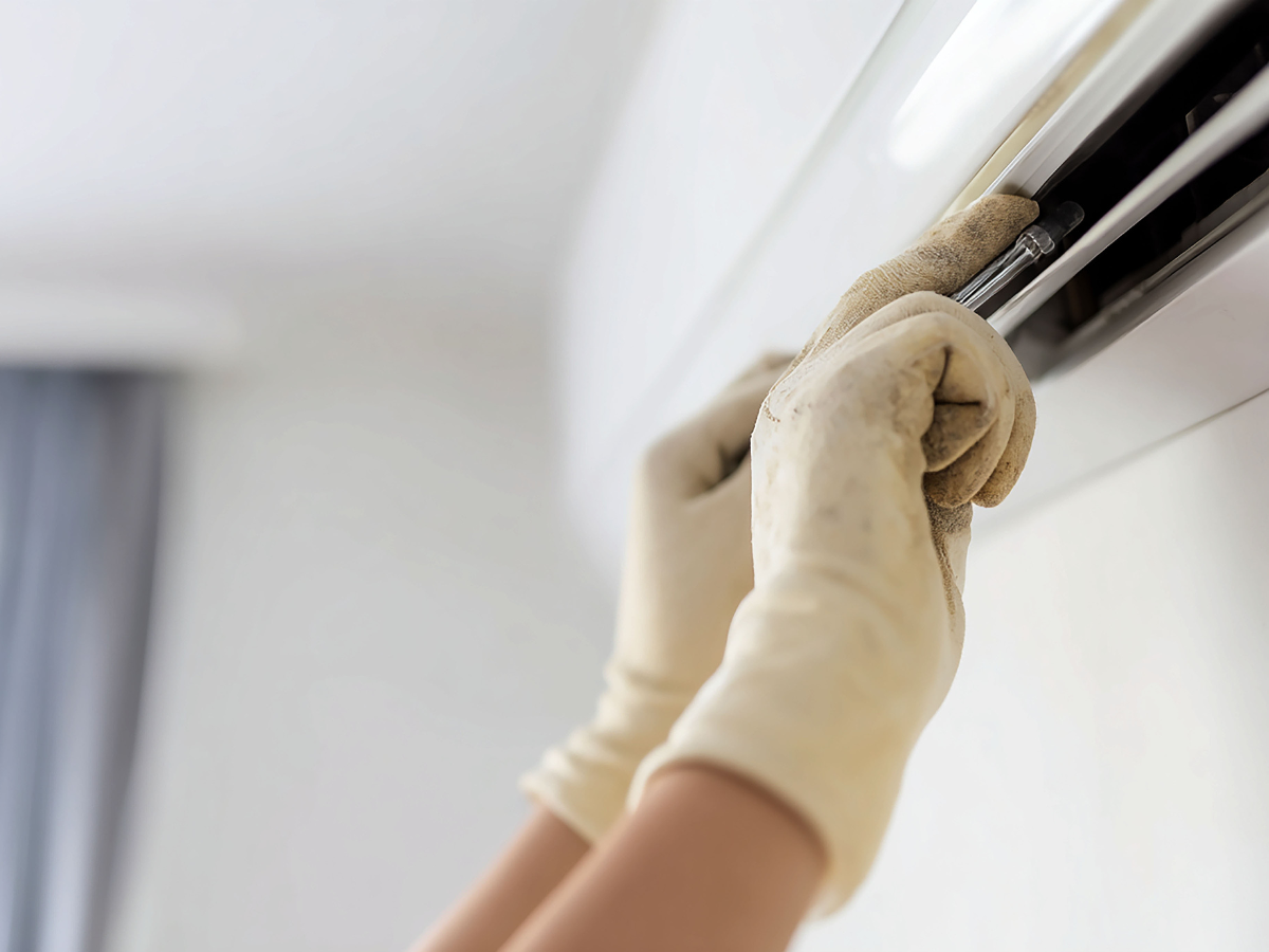 Hands in gloves cleaning an air conditioner vent.