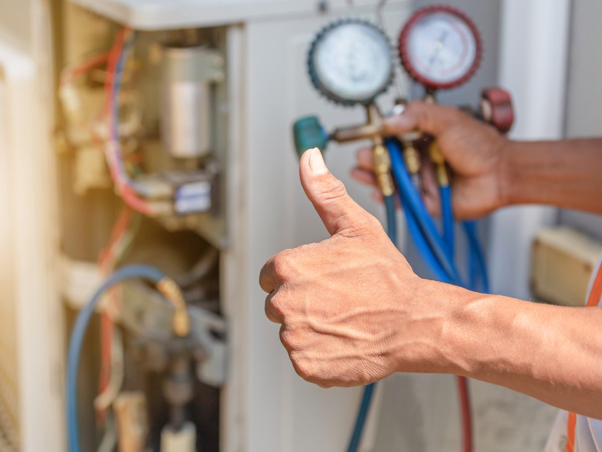 HVAC technician with thumbs up, checking an air conditioning unit using gauges.