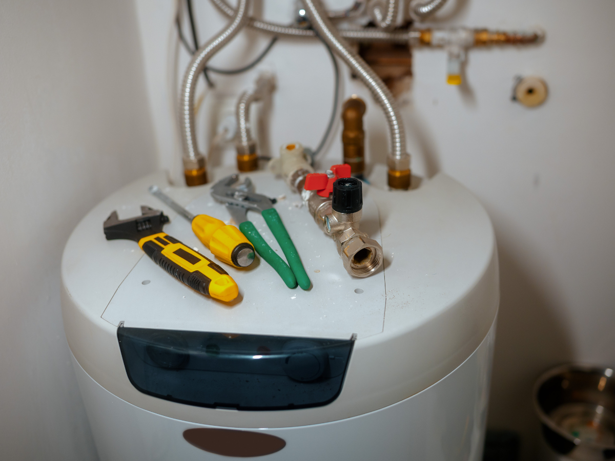 Water heater with tools on top: wrench, pliers, screwdriver, valve. White tank.