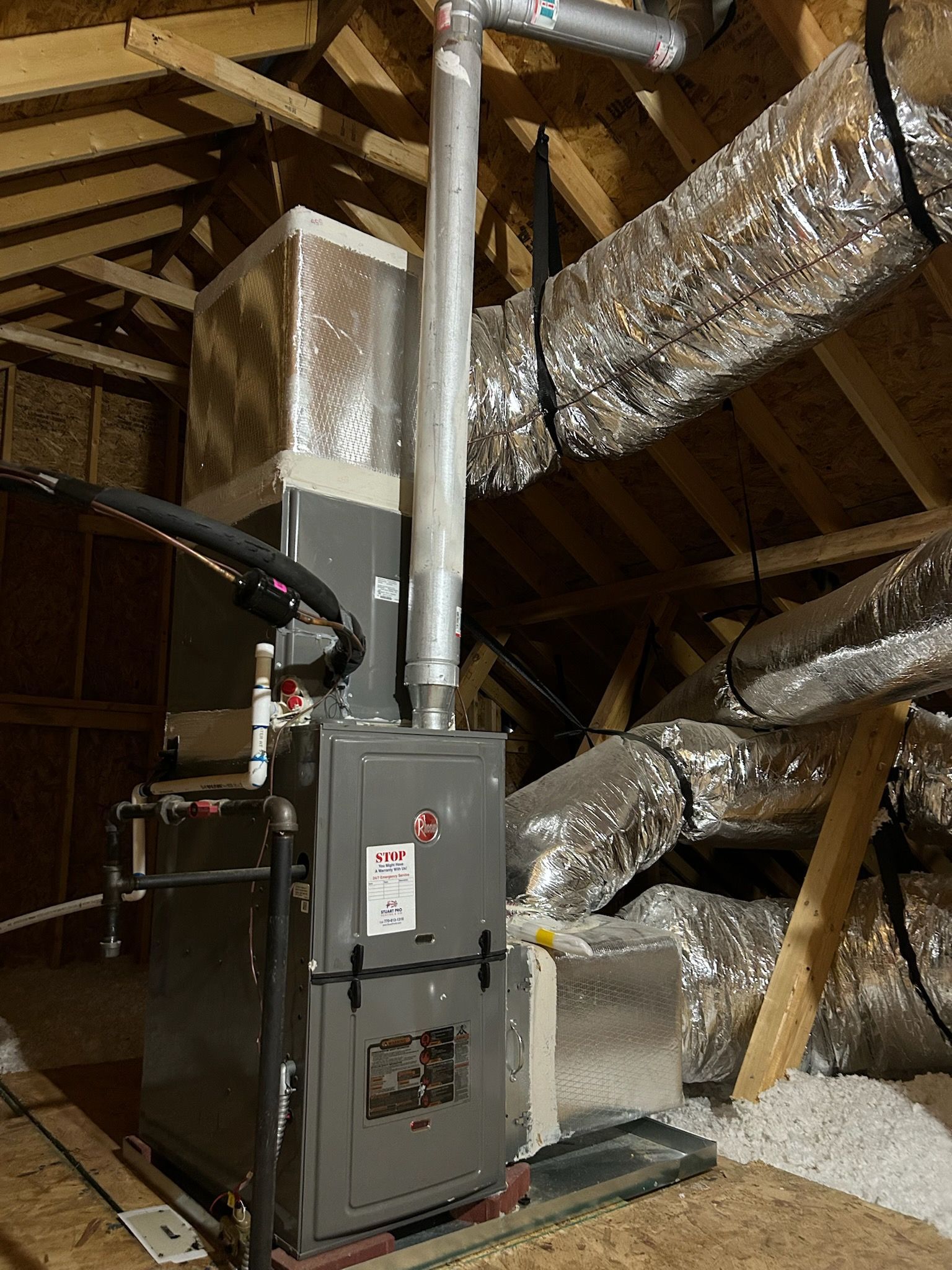 Furnace and ductwork in an attic, with metallic pipes and insulated vents.