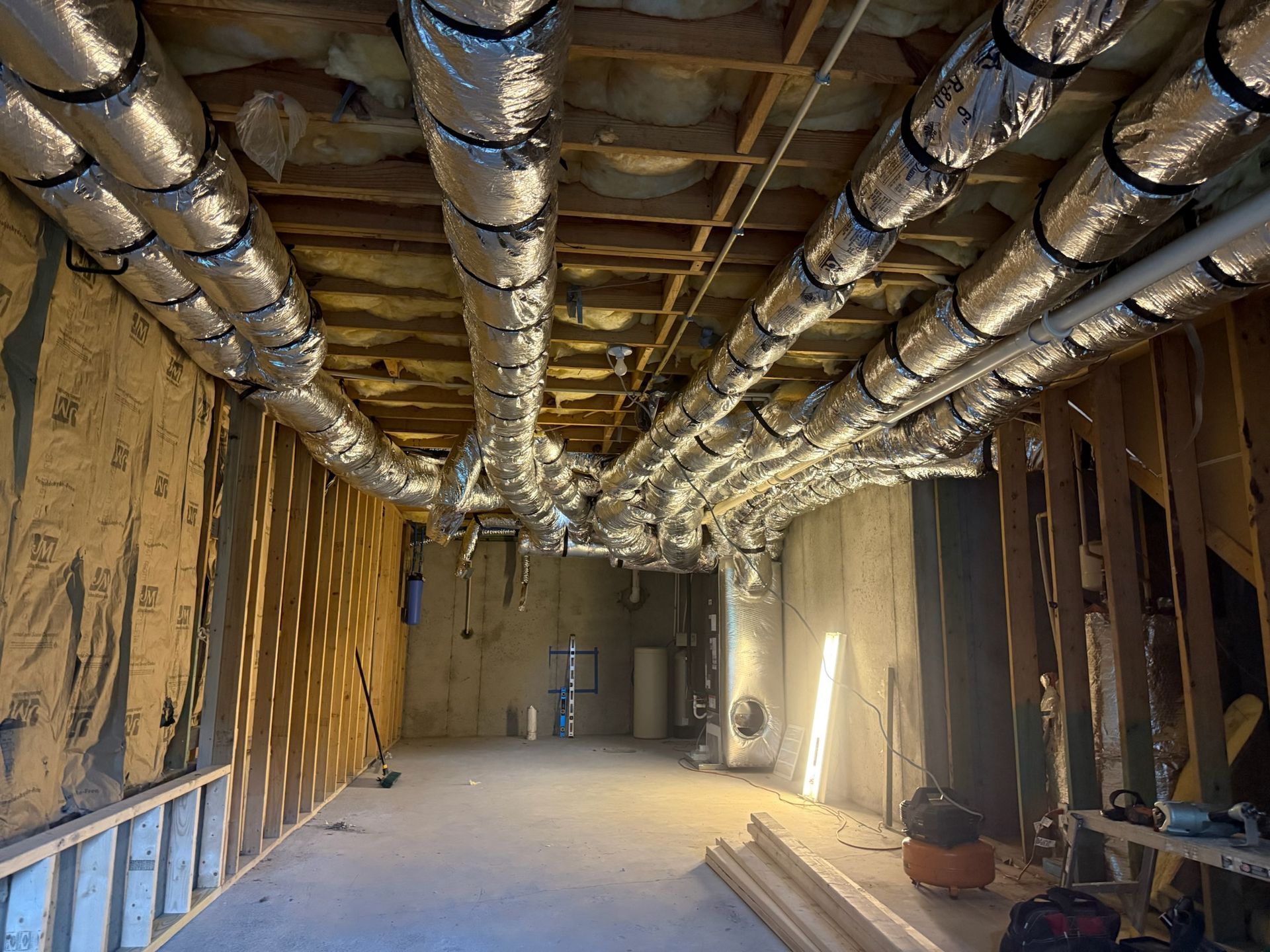 Unfinished basement with silver ductwork, wooden framing, and exposed insulation.