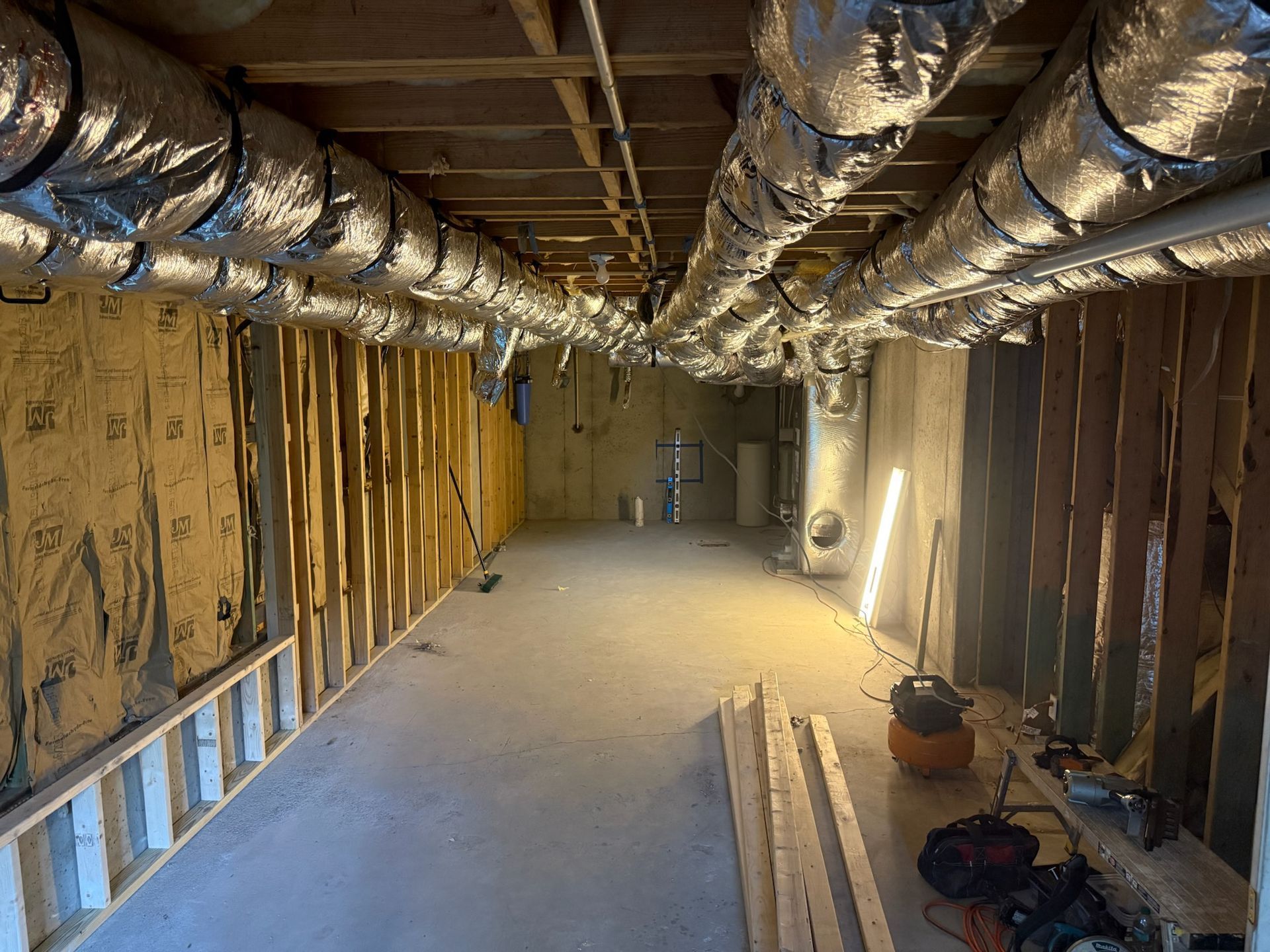 Basement under construction, with wooden framing, ductwork, insulation, and concrete floor.